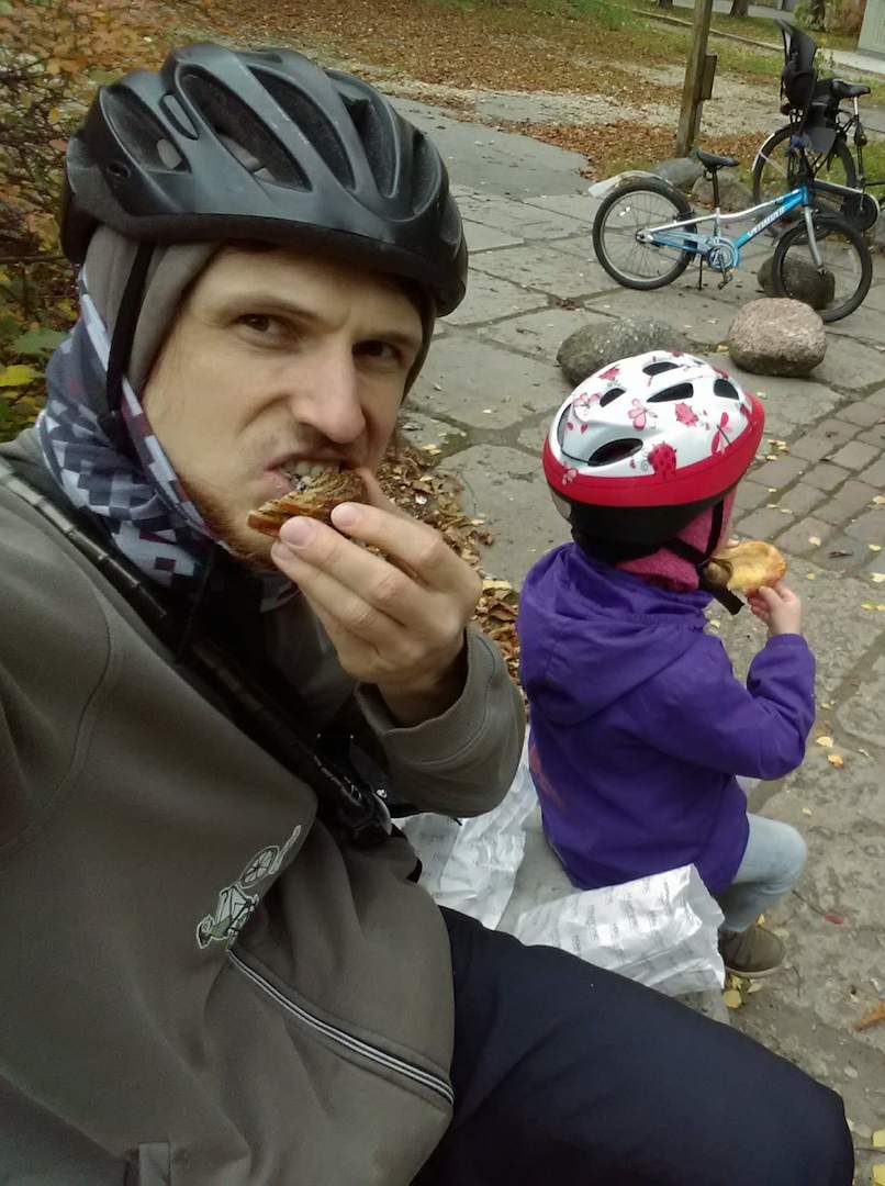 Reinis nyder en snack sammen med sit barn på en cykeltur, hvor de begge har cykelhjelm på udendørs.
