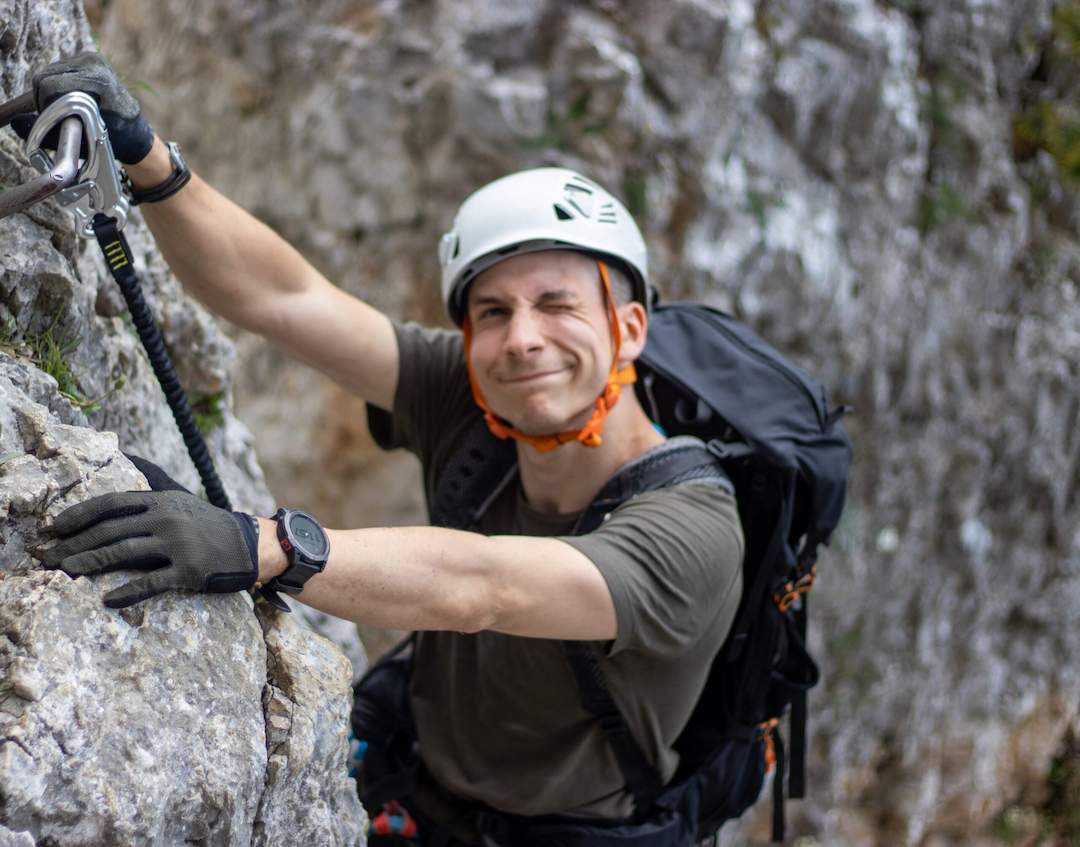 Michał climbing a rocky route wearing a helmet, gloves, and backpack.