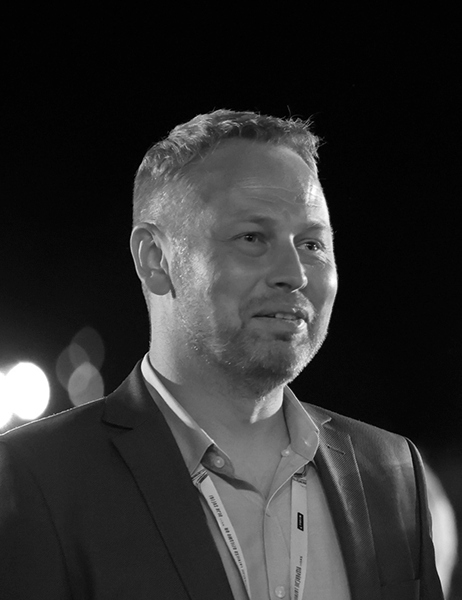Ilmars wearing a suit and conference lanyard during an evening event.